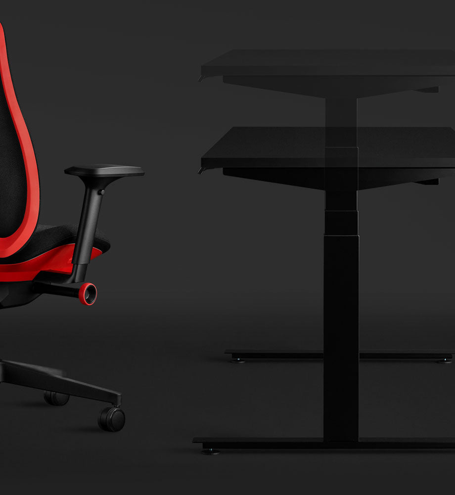 Sidovy av ett svart Nevi-spelbord och en röd Vantum-spelstol från Herman Miller, som visar bordets sit-stand-funktion.