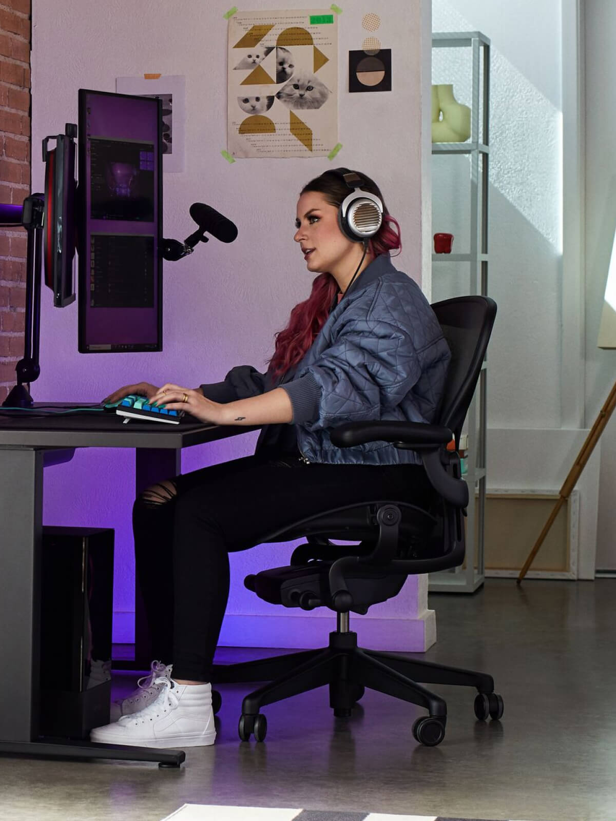 Electra spelar sittande på Aeron i onyx svart med Nevi-spelbord i svart och Ollin-monitorarm