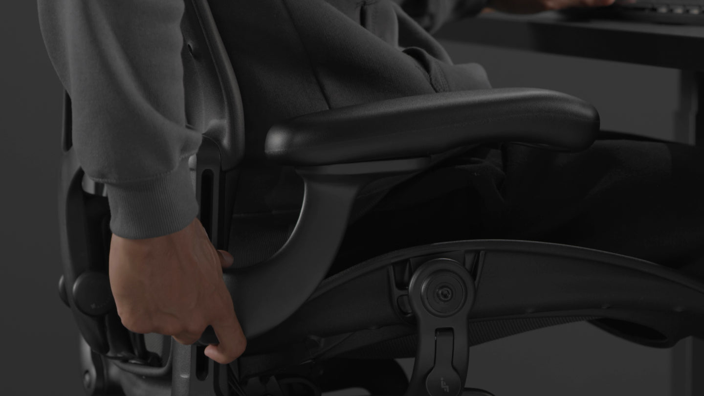 En video av en person som sitter i en svart Aeron-spelstol från Herman Miller och sträcker sig bredvid stolen för att justera armstöden.
