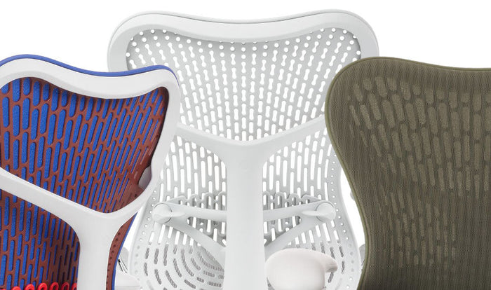 Närbild av tre Mirra 2-kontorsstolar från Herman Miller, som visar de tillgängliga färgerna. Den första är blå, orange och vit, den andra är endast vit och den tredje är grön.