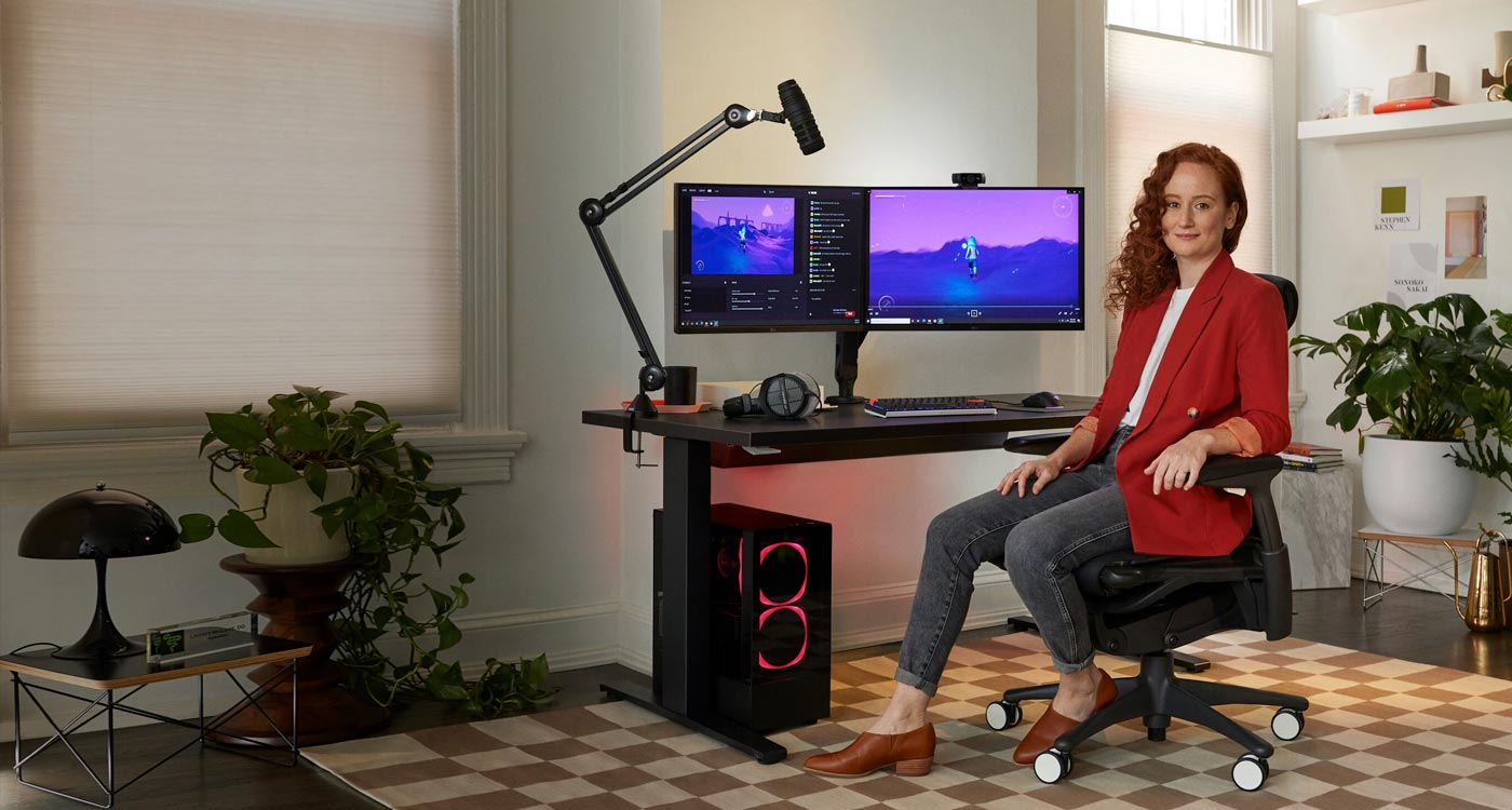 Foto av Dr Lindsey Migliore sittande i en Embody gaming chair vänd mot kameran med Nevi gaming desk i svart med ollin monitor arms