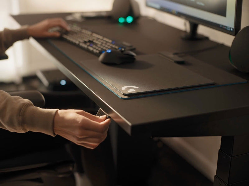 En video av en person som sitter vid ett svart Nevi-spelbord från Herman Miller och trycker på en knapp för att sänka skrivbordet.
