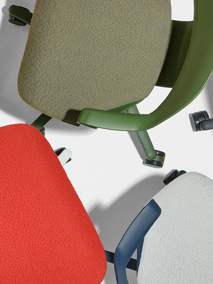 Ovanifrånvy av tre Herman Miller Zeph-kontorsstolar i grönt, rött och blått, som visar texturen på sittdynorna.