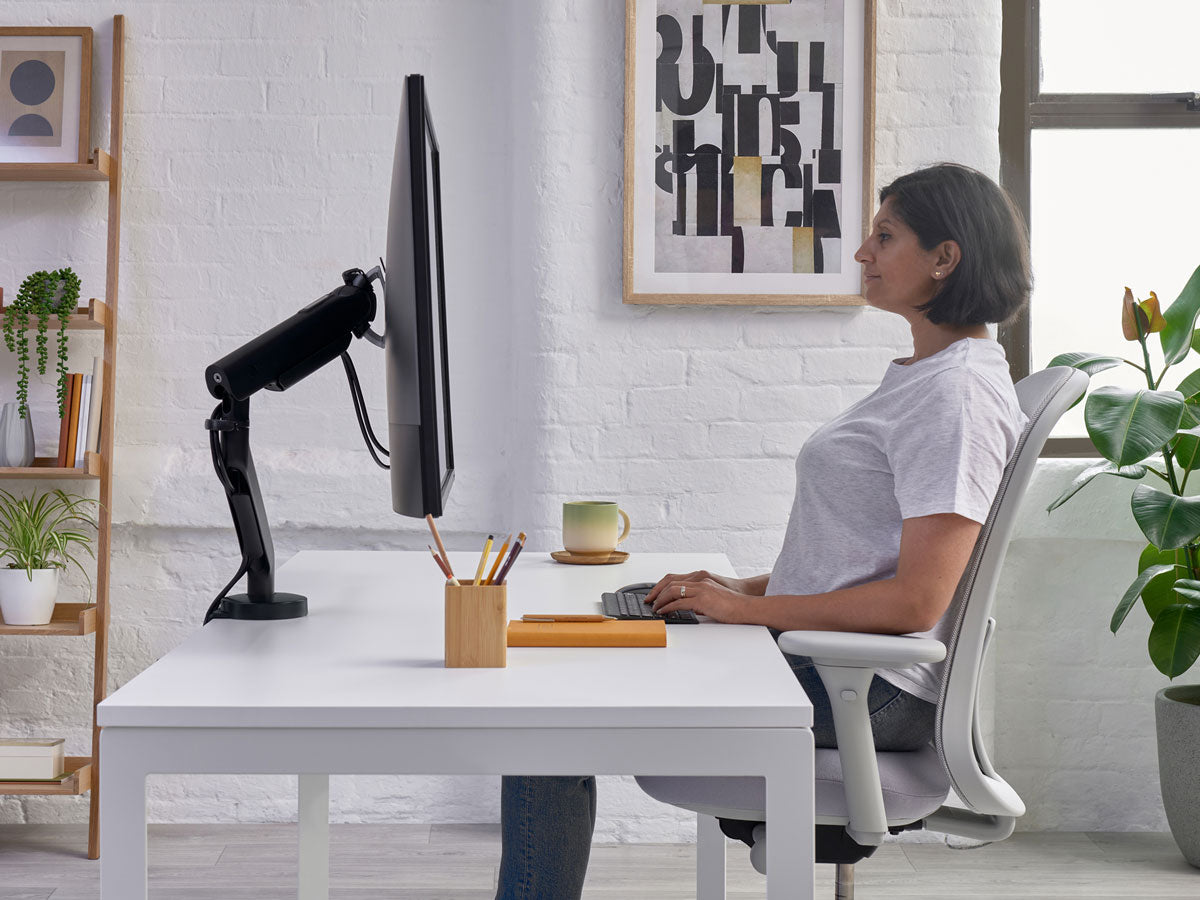 Kvinna sitter vid skrivbord i kontorsstol Lino i mineralvit med grå sits och visar handledsnivån på skrivbordet som en del av korrekt sittställning