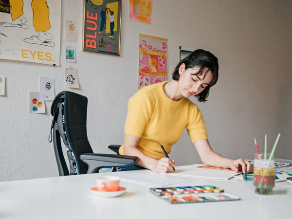Illustratör, målare och författare Molly Rose Dyson arbetar i sin ateljé, sittande i en Embody-gamingstol i svart och cyanblått