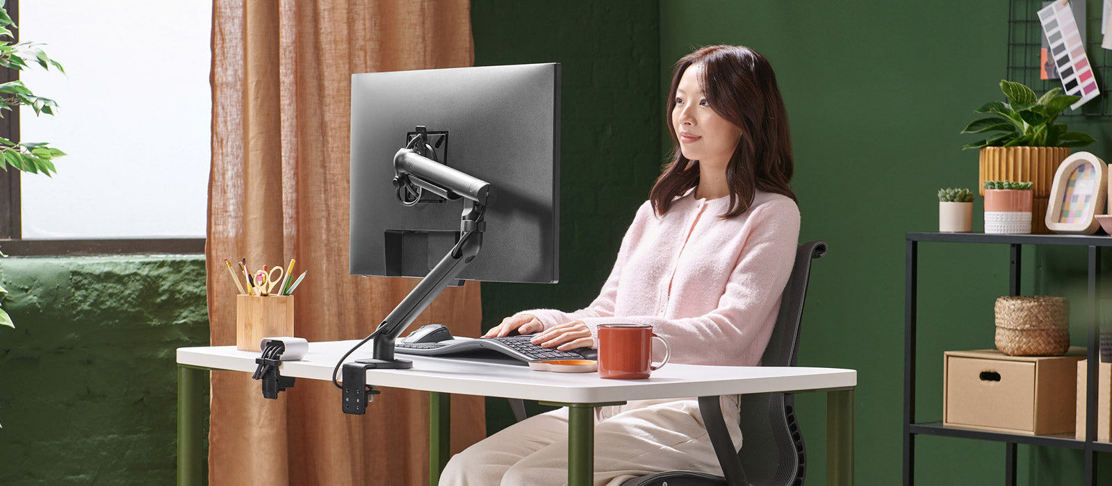 En kvinna satt vid ett Herman Miller OE1-skrivbord och arbetade vid en skärm som hölls uppe av en svart Flo-skärmarm.