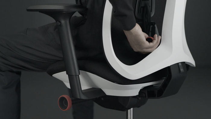 En video av en person som sitter i en vit och svart Vantum-spelstol från Herman Miller och sträcker sig bakom stolen för att justera ryggstödet.