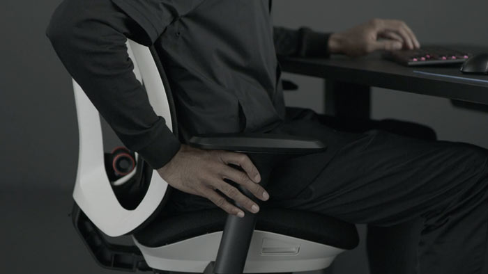 En video av en person som sitter i en vit och svart Vantum-spelstol från Herman Miller och sträcker sig bredvid stolen för att justera armstöden.