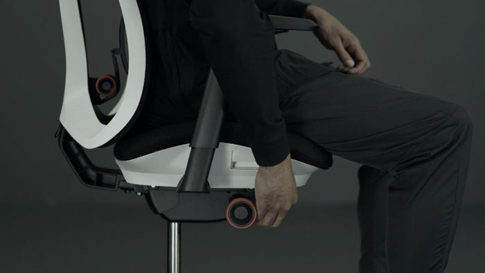 En video av en person som sitter i en vit och svart Vantum-spelstol från Herman Miller och sträcker sig bredvid stolen för att justera sitthöjden.
