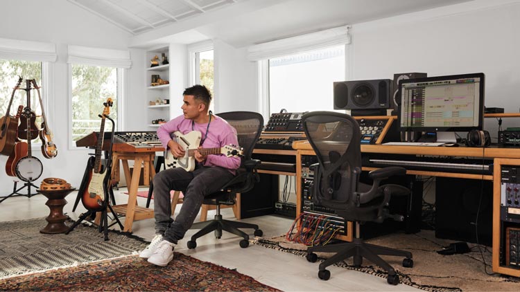 Foto av Rostam, musiker, producent och kompositör, i sin musikstudio där han spelar gitarr sittande i kontorsstolen Aeron i grafit