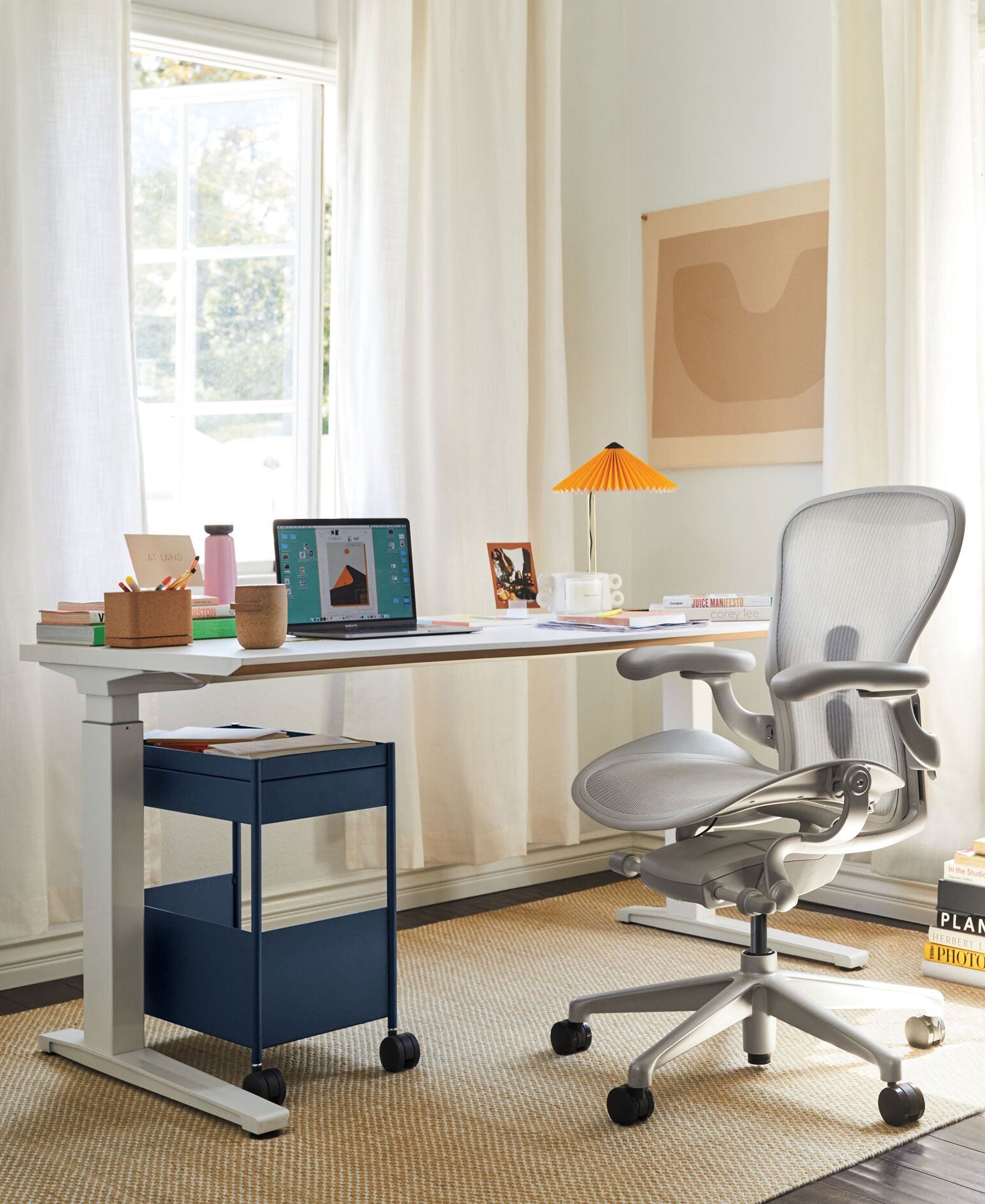Hemmakontor med Aeron kontorsstol i mineralvit, med Jarvis sit-stand-skrivbord i vitt. Tillbehören inkluderar Oripura laptopstativ och Hay Matin bordslampa