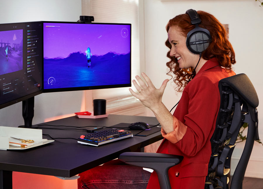 Foto av Dr Lindsey Migliore som ler medan hon spelar dataspel i Embody cyan gaming chair med Nevi gaming desk i svart