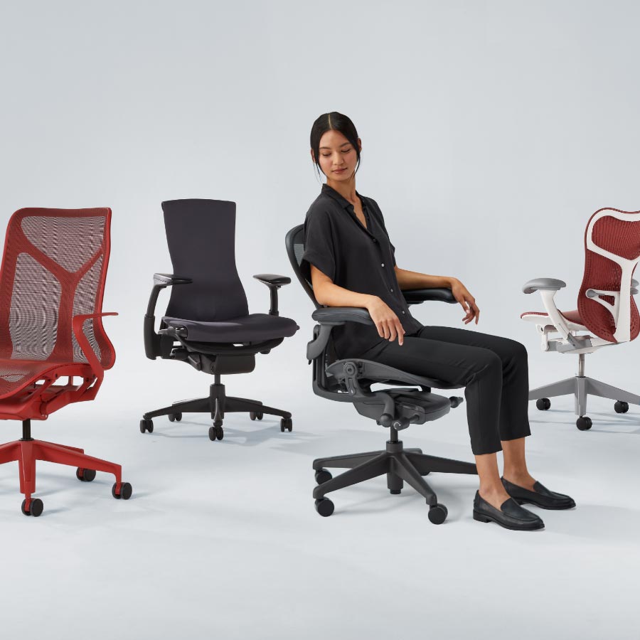 Fyra Herman Miller kontorsstolar i rad, inklusive Cosm med mellanhög rygg i canyonröd, Embody i svart, Aeron i grafit med en kvinna sittande och slutligen Mirra 2 med vit ram och röd sits och rygg