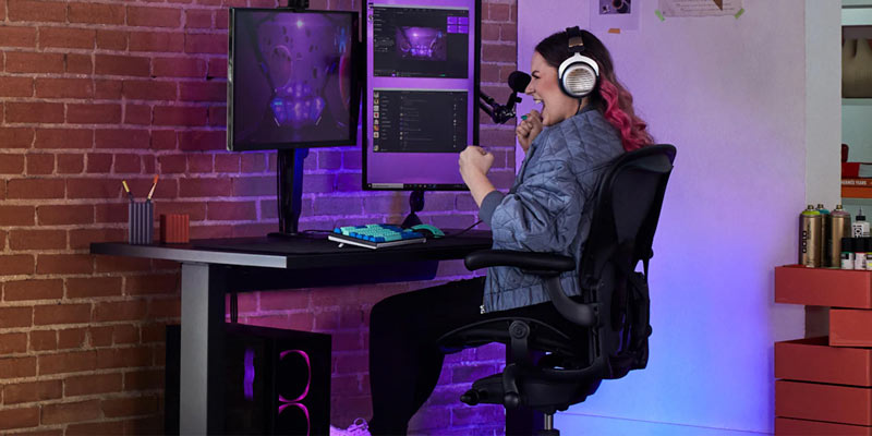 Electra ler med knutna nävar medan hon spelar i Aeron gaming onyx black med Nevi gaming desk i svart och Ollin-monitorarm