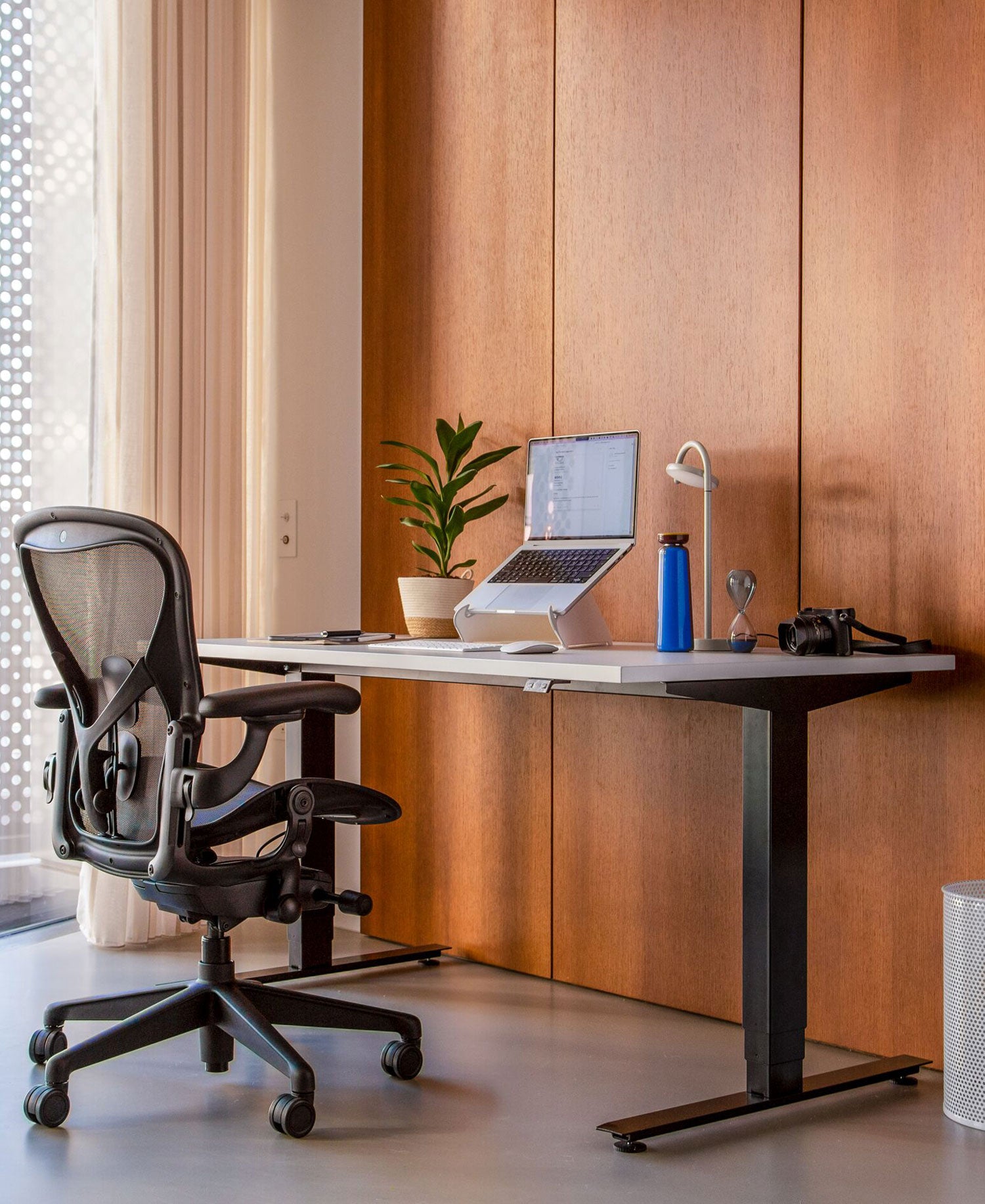 Hemmakontor med Aeron kontorsstol i grafit framför Nevi sit-stand-skrivbord med svarta ben och vit skiva och Oripura laptopstativ.