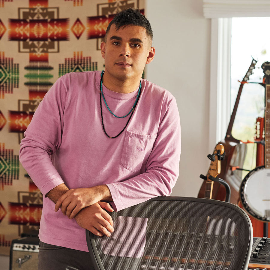 Foto av Rostam, musiker, producent och kompositör, stående lutad mot en Aeron kontorsstol i grafit med musikinstrument i bakgrunden
