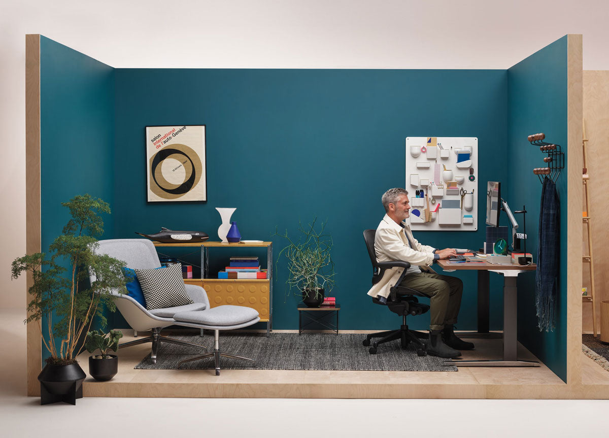 Man sittande i hörnet av ett hemmakontor med Aeron-kontorsstol i grafit framför ett Jarvis sit-stand-skrivbord med svarta ben och träskiva
