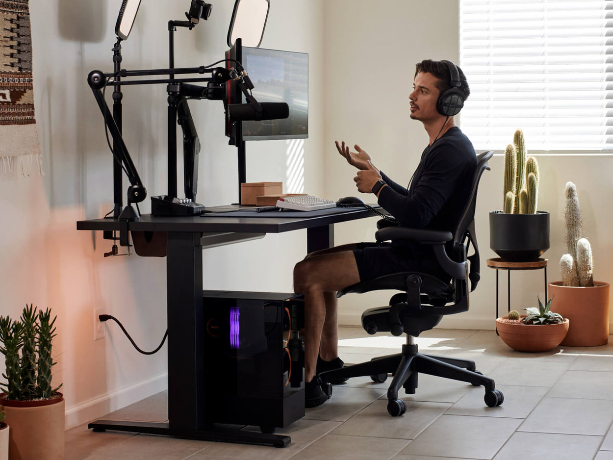 Gamern Xaryu sitter vid sin gaming-station med en Aeron-gamingstol i grafit, ett Nevi-gamingbord och dubbla monitorarmar från Ollin