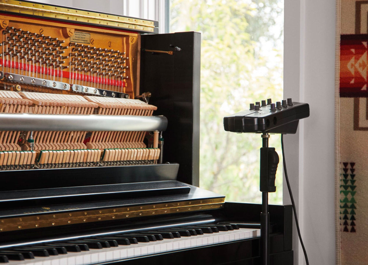 Ett upprättstående piano med öppen front och ljudinspelningsutrustning bredvid.